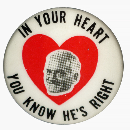 Round, white button with a red heart at the center and a grayscale portrait of Barry Goldwater at its center. Black text reading "In Your Heart You Know He's Right", which encircles the portrait. 