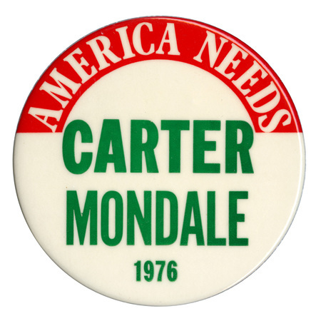 Round, white button with a red band along the top edge. White and green text reads "AMERICA NEEDS CARTER MONDALE 1976"