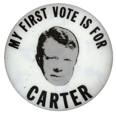 Round, silver button with a black and white portrait of Jimmy Carter. Black text reads "MY FIRST VOTE IS FOR CARTER"