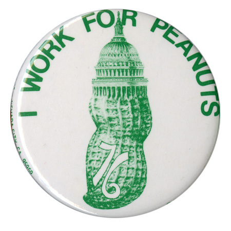Round, white button with a green image of a peanut topped by the dome of the US Capitol. Green text reads "I WORK FOR PEANUTS 76"