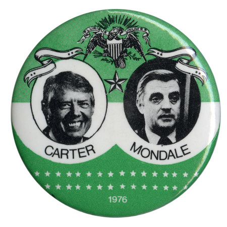 Round, green and white button with black and white photographs of Jimmy Carter and Walter Mondale surrounded by drawings of an eagle holding a shield, ribbons, and stars. Black and white text reads "CARTER MONDALE 1976"