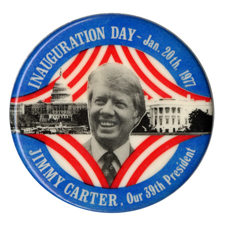 Round button with black and white photographs of Jimmy Carter, the US Capitol building, and the White House surrounded by red and white stripes and a blue border. White text reads "INAUGURATION DAY - Jan. 20th, 1977 JIMMY CARTER, Our 39th President"