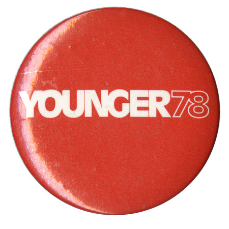 Round, red button with white text reading "YOUNGER 78"