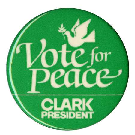 Round, green button with a white drawing of a dove holding an olive branch. White text reads "Vote for Peace CLARK PRESIDENT"
