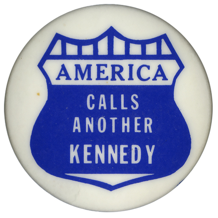 Round, white button with a blue drawing of a shield. Blue and white text within the shield reads "AMERICA CALLS ANOTHER KENNEDY"