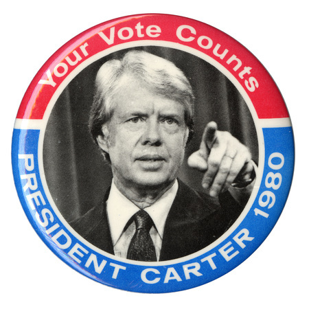 Round button with red and blue border and black and white photograph of Jimmy Carter in the center. White text around the edge reads "Your Vote Counts PRESIDENT CARTER 1980"