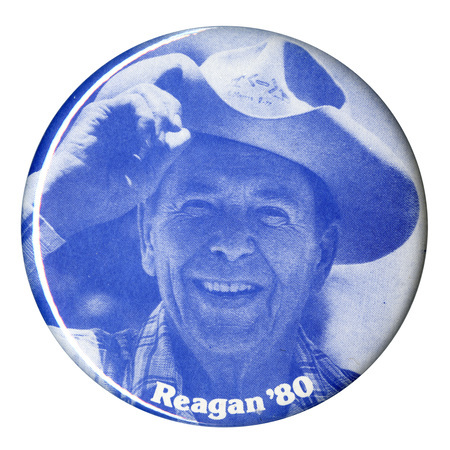 Round, blue button with a photograph of Ronald Reagan wearing a cowboy hat. White text reads "Reagan '80"