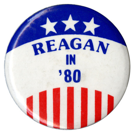 Round, white button with blue and red stars and stripes. Blue text reads "REAGAN IN '80"