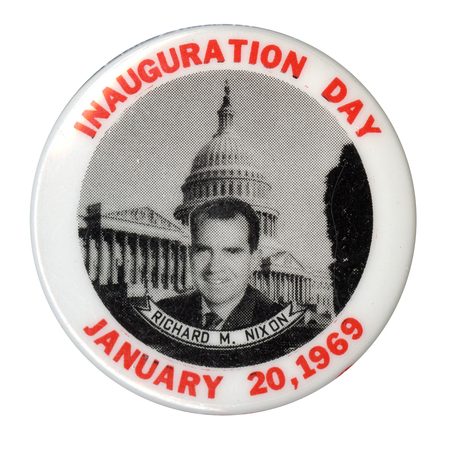 Round, white button with a black and white portrait of Richard Nixon in front of the US Capitol. Underneath Nixon's portrait is a ribbon with the text "Richard M. Nixon." Around the edge of the button is red text reading "Inauguration Day, January 20, 1969."