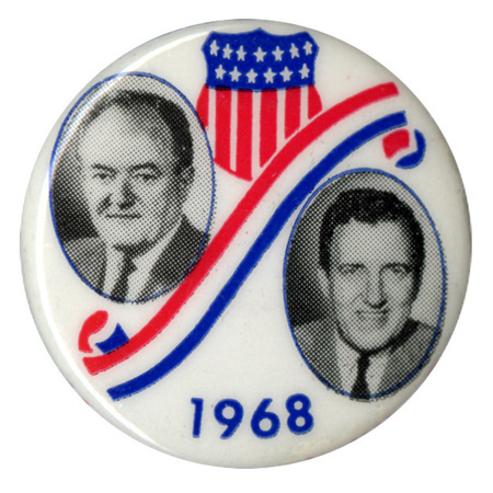 Round, white button with portraits of Hubert Humphrey and Edmund Muskie and red, white, and blue shield and ribbon decorations. Text reads "1968."
