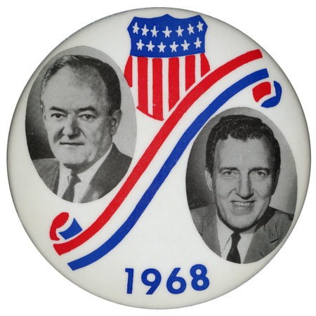 Round, white button with portraits of  Hubert Humphrey and Edmund Muskie surrounded by red, white, and blue shield and ribbon decorations and the text "1968."