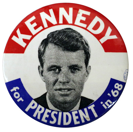 Round, white button with a portrait of Robert F. Kennedy. Red and blue bands along the edge of the button contain white text reading "Kennedy for President in '68."