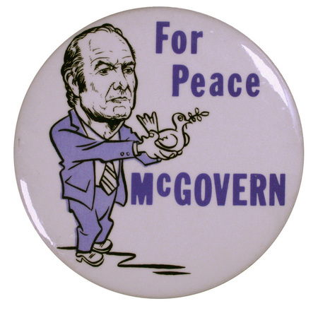 Round, white button with a caricature drawing of George McGovern holding a white dove with an olive branch in its mouth. Blue text reads "For Peace McGOVERN"
