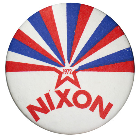 Round, white button with stylized red star with blue and red stripes emerging from it. Red text reads "1972 NIXON"