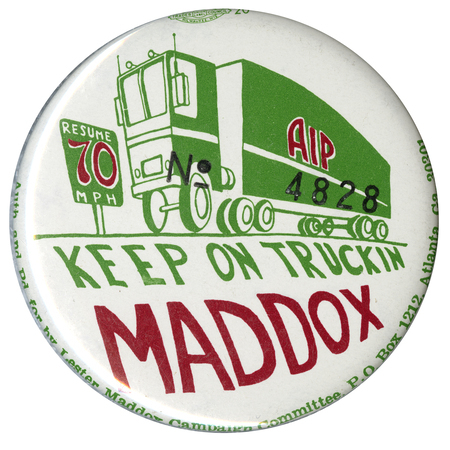Round, white button with a drawing of a green semi truck with the letters "AIP" on its side and a green and brown sign reading "RESUME 70 MPH." Green and brown text below reads "KEEP ON TRUCKIN MADDOX". Black text stamped on the button reads "No 4828"