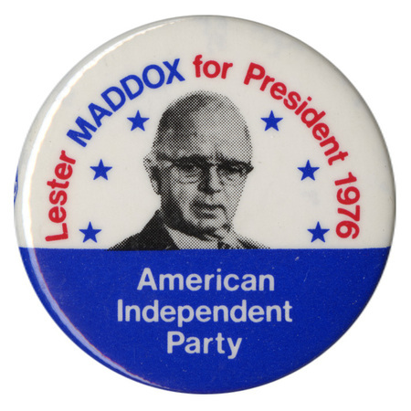 Round, white and blue button with a black and white portrait of Lester Maddox surrounded by six blue stars. Red, blue, and white text reads "Lester MADDOX for President 1976 American Independent Party"