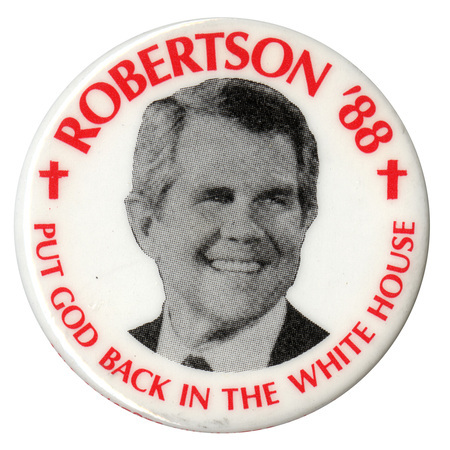 Round, white button with a black and white photograph of Pat Robertson flanked by two red Christian crosses. Red text reads "ROBERTSON '88 PUT GOD BACK IN THE WHITE HOUSE"