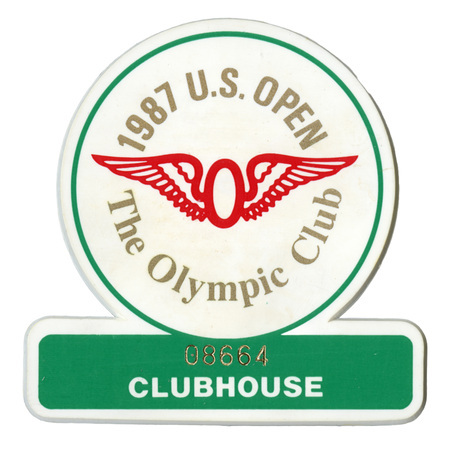 Button in the shape of a circle sitting atop a broad rectangle. Within the white circle is the red, winged symbol of the Olympic Club in San Francisco and gold text reading "1987 U.S. OPEN The Olympic Club." Within the green rectangle is gold and white text reading "08664 CLUBHOUSE"