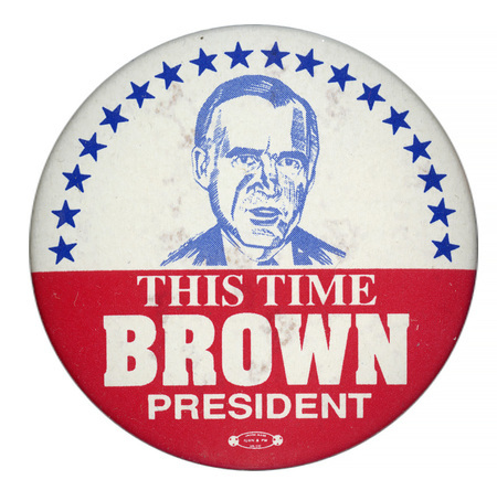 Round, white and red button with a blue drawing of Jerry Brown surrounded by a border of blue stars. White text in the red lower half of the button reads "THIS TIME BROWN PRESIDENT"