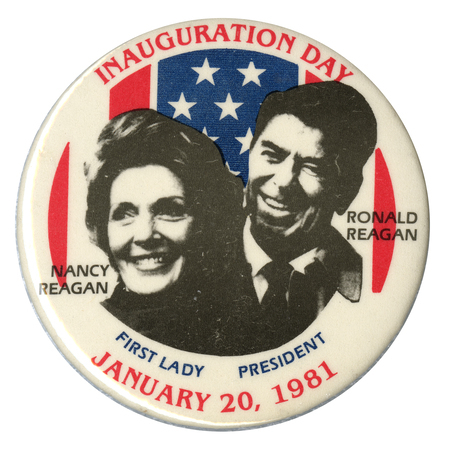 Round, white button with black and white photographs of Nancy and Ronald Reagan against red and blue stars and stripes decorations. Red and black text reads "INAUGURATION DAY JANUARY 20, 1981 NANCY REAGAN FIRST LADY RONALD REAGAN PRESIDENT"