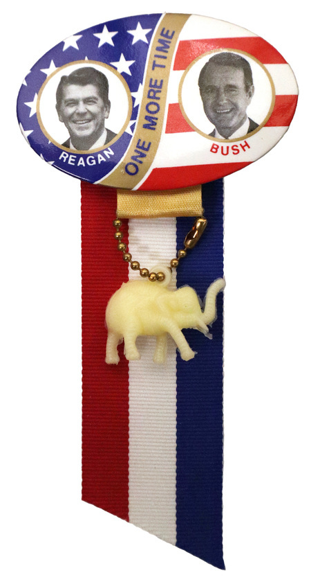 Oval button with red, white, and blue stars and stripes decorations and black and white portraits of Ronald Reagan and George H. W. Bush. Text reads "REAGAN BUSH ONE MORE TIME". Attached to the bottom of the button is a red, white, and blue ribbon and a yellowed plastic elephant.
