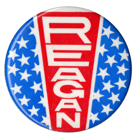 Round button with white stars on a blue field and a vertical red sign reading "REAGAN"