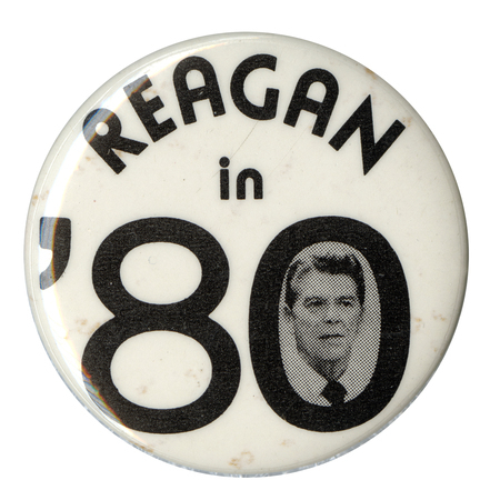 Round, white button with black text reading "REAGAN in '80." A black and white photograph of Ronald Reagan appears in the "0" of "'80"