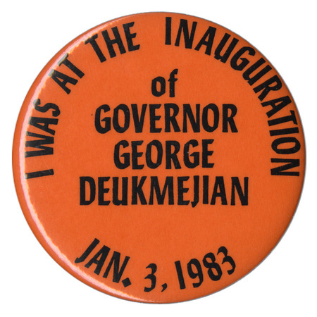 Round, orange button with black text reading "I WAS AT THE INAUGURATION of GOVERNOR GEORGE DEUKMEJIAN JAN. 3, 1983"