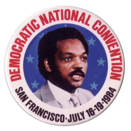 Round button with a white border and a color photograph of Jesse Jackson surrounded by blue stars. Red and black text reads "DEMOCRATIC NATIONAL CONVENTION SAN FRANCISCO JULY 16-19 1984"