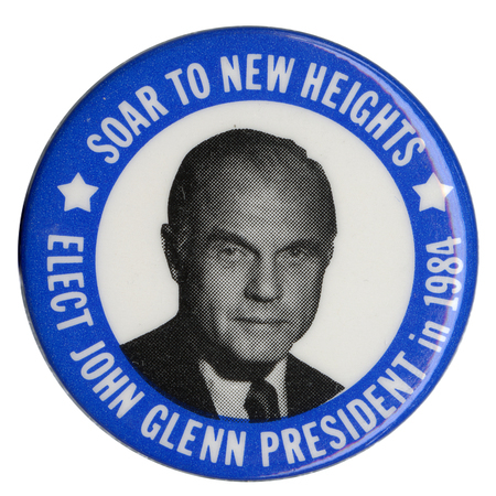 Round button with a blue border and a black and white photograph of John Glenn in a white circle in the center. White text reads "SOAR TO NEW HEIGHTS ELECT JOHN GLENN PRESIDENT in 1984"
