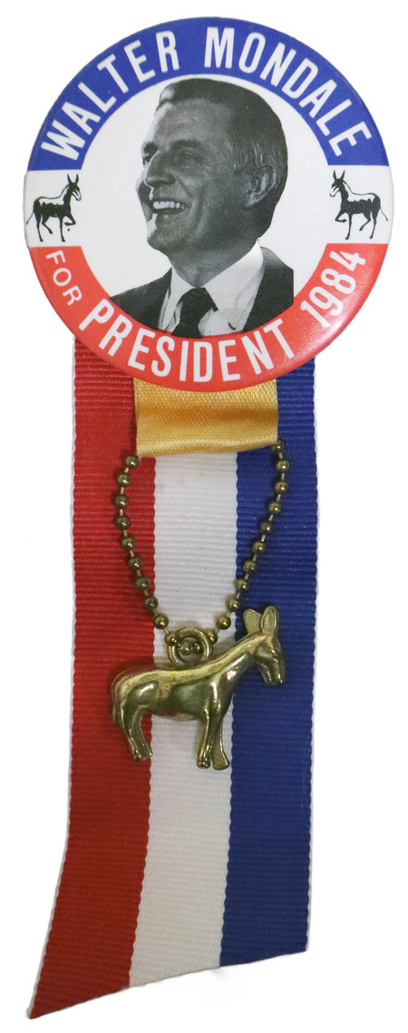 Round button with a red and blue border and a black and white photograph of Walter Mondale flanked by drawings of two black donkeys. White text reads "WALTER MONDALE FOR PRESIDENT 1984." Attached to the bottom of the button is a red, white, and blue ribbon and a gold donkey charm.