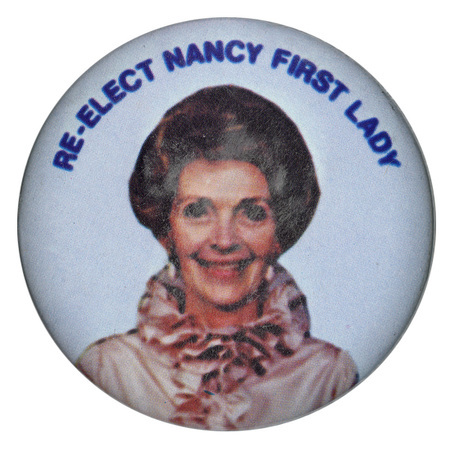 Round, white button with a color photograph of Nancy Reagan. Blue text reads "RE-ELECT NANCY FIRST LADY."