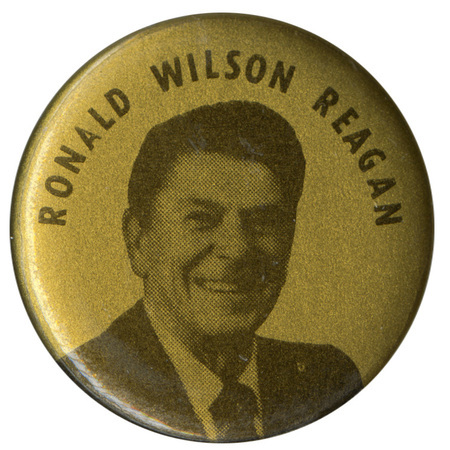 Round, gold button with a black and white photograph of Ronald Reagan and black text reading "RONALD WILSON REAGAN"