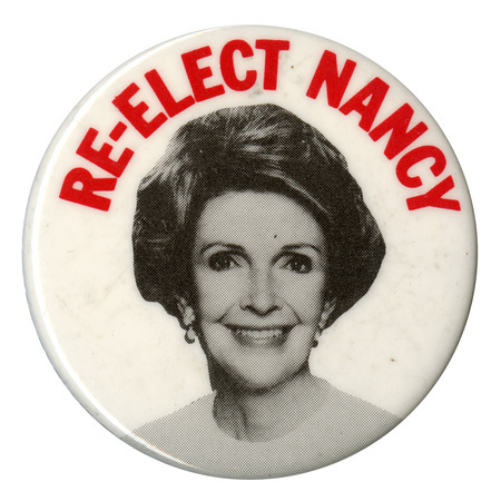 Round, white button with a black and white photograph of Nancy Reagan. Red text reads "RE-ELECT NANCY"