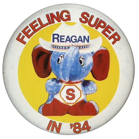 Round button with a white border and a drawing of a stuffed blue elephant wearing a cowboy hat labeled "REAGAN" and an "S" on its chest. Red text reads "FEELING SUPER IN '84"