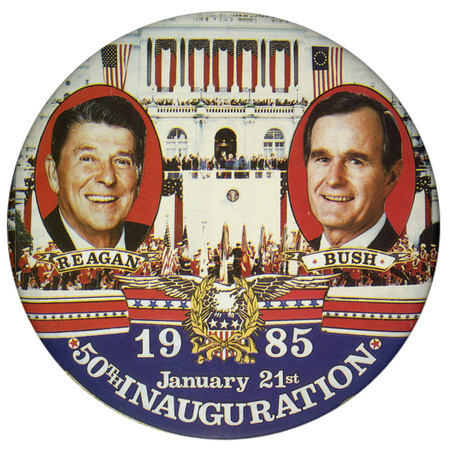 Round button with color photographs of Ronald Reagan and George H. W. Bush against a color photograph of the US Capitol. On the lower part of the button is an elaborate decoration with an eagle,  and scrollwork. White text reads "1985 January 21st 50th INAUGURATION"