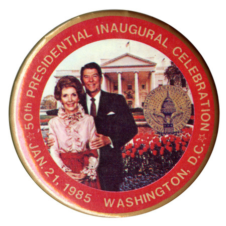 Round button with a red border and a color photograph of Nancy and Ronald Reagan with the White House, a seal, and flowers in the background. Gold text reads "50th PRESIDENTIAL INAUGURAL CELEBRATION JAN. 21, 1985 WASHINGTON, D.C."