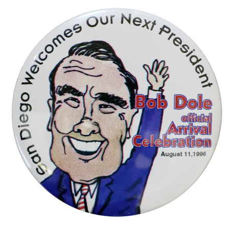 Round, white button with a color illustration of Bob Dole wearing a blue suit and waving. Black and red text reads "San Diego Welcomes Our Next President Bob Dole official Arrival Celebration August 11, 1996"