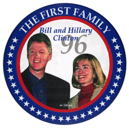 Round button with a red and blue border with white stars. In the center is a color photograph of Bill Clinton and Hillary Clinton. White, blue, and gray text reads "THE FIRST FAMILY Bill and Hillary Clinton 96"