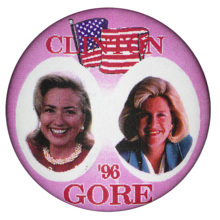 Round, pink button with a color illustration of a US flag and color photographs of Hillary Clinton and Tipper Gore. Red text reads "CLINTON '96 GORE"