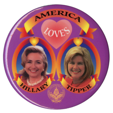 Round, purple button with color photographs of Hillary Clinton and Tipper Gore inside red and yellow frames below a pink heart. Black text reads "AMERICA LOVES HILLARY TIPPER"