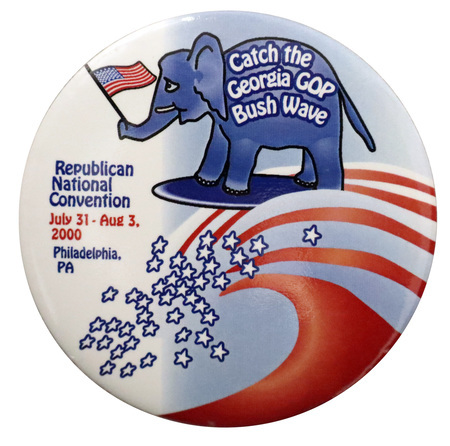 Round, blue and white button with an illustration of a blue elephant holding a US flag with its trunk riding a blue surfboard on a wave composed of red and white stripes and blue and white stars. On the elephant's side, white text reads "Catch the Georgia GOP Bush Wave". Blue and red text on the button reads "Republican National Convention July 31-Aug 3, 2000 Philadelphia, PA"