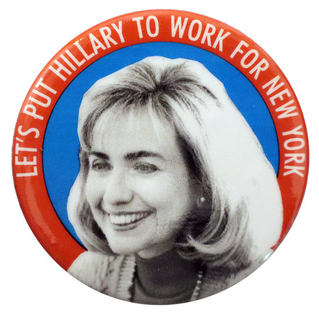 Round button with a red border and a blue center, on which is a black and white photograph of Hillary Clinton. White text reads "LET'S PUT HILLARY TO WORK FOR NEW YORK"