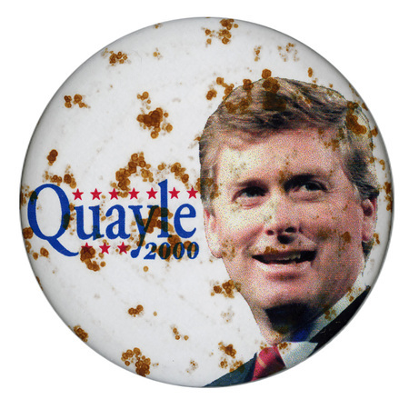 Round, white button mottled with patches of  brown oxidation. In the center is a color photograph of Dan Quayle. Blue text reads "Quayle 2000"