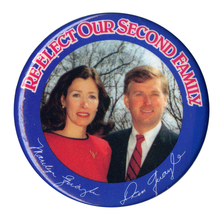 Round button with a blue border and a color photograph of Marilyn and Dan Quayle in the center, above their autographs in white. Red and white text at the top of the button reads "RE-ELECT OUR SECOND FAMILY"