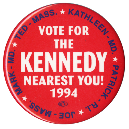 Round, red button with white text in the center reading "VOTE FOR THE KENNEDY NEAREST YOU! 1994" Blue text around the edge of the button reads "KATHLEEN - MD. PATRICK R. I. JOE - MASS. MARK - MD. TED - MASS."