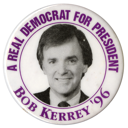 Round, white button with a black and white photograph of Bob Kerrey in the center. Purple text reads "A REAL DEMOCRAT FOR PRESIDENT BOB KERREY '96"