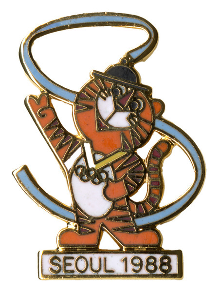 Enameled pin in the shape of a tiger surrounded by a blue ribbon and standing on a white rectangle with black text reading "SEOUL 1988"