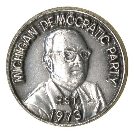 Round, silver pin with an embossed illustration of a person and text reading "MICHIGAN DEMOCRATIC PARTY 1973"
