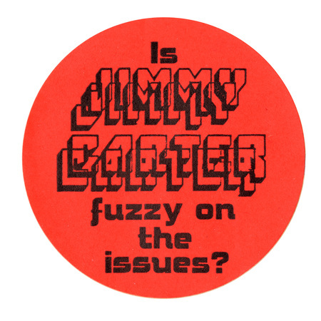 Round, orange sticker with black text reading "Is JIMMY CARTER fuzzy on the issues?" The words "JIMMY CARTER" are intentionally made difficult to read with jumbled, layered text.